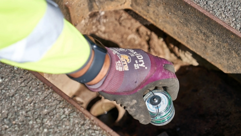 Utility worker using digital sensor to detect water leak underground